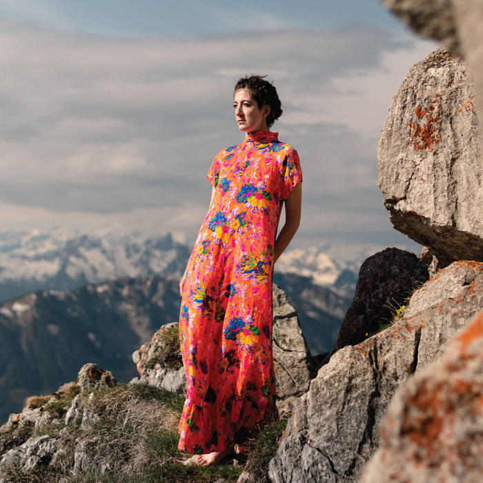 album cover is a photograph of the artist in a long floral dress standing on rocky ground with mountaintops and sky in the background