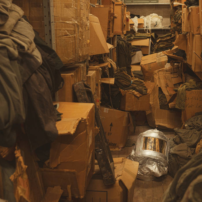 image is a photograph of a small room packed with cardboard boxes and clutter